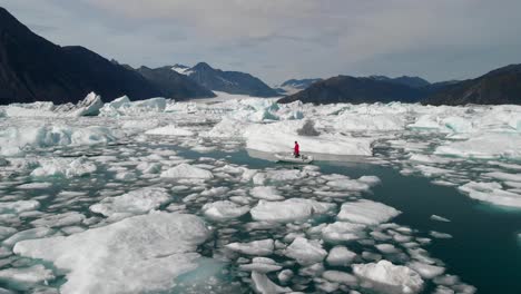 Hombre-Navegando-En-El-Lago-Con-Trozos-De-Hielo-Flotando-Con-Montañas-Cubiertas-De-Nieve-En-El-Fondo-En-Glacier-Bay,-Alaska
