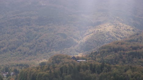 Berghütte-Auf-Dem-Gipfel-Eines-Berges-In-Den-Alpen-Und-Lichtstrahl,-Der-Durch-Die-Wolken-Dringt-Und-Die-Herbstfarben-Und-Das-Haus-Auf-Dem-Hügel-Erhellt
