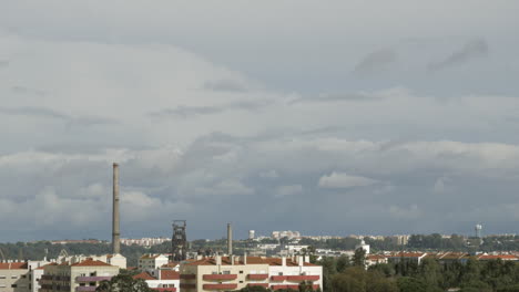 Nubes-Blancas-Moviéndose-Sobre-Edificios-Urbanos-Y-Chimeneas-De-Fábricas.
