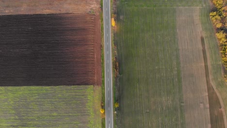 Aerial-view-of-a-road,-in-middle-of-colorful-fields,-sunny,-autumn-day---reverse,-tilt,-drone-shot