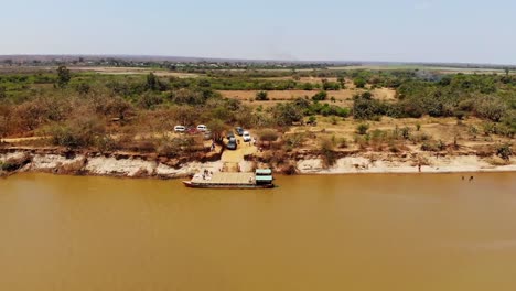 Cars-wait-to-board-a-river-ferry-to-cross-the-Tsiribihina-River-in-Madagascar,-Aerial-view-drone-wide-shot