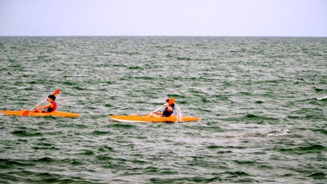 A-young-skilled-couple-kayaking-in-the-middle-of-a-calm-sea-at-summertime-in-Bombas-and-Bombinhas-beaches,-Brazil