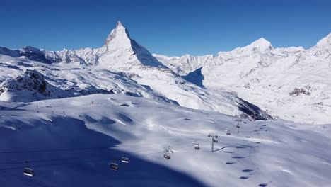Esquiadores-En-La-Pista-De-Esquí-Blanca-Frente-Al-Hermoso-Matterhorn-En-Suiza,-Cielo-Azul