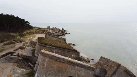 Aerial-view-of-abandoned-seaside-fortification-building-at-Karosta-Northern-Forts-on-the-beach-of-Baltic-sea-in-Liepaja-in-overcast-spring-day,-wide-establishing-drone-ascending-shot-moving-forward