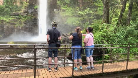 Tourist-family-in-COVID-masks-enjoy-view-of-waterfall-from-footbridge