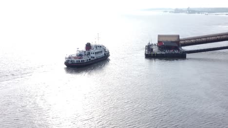 Aerial-view-following-Mersey-commuter-passenger-ferry-in-shimmering-river-arriving-Woodside-station-Birkenhead