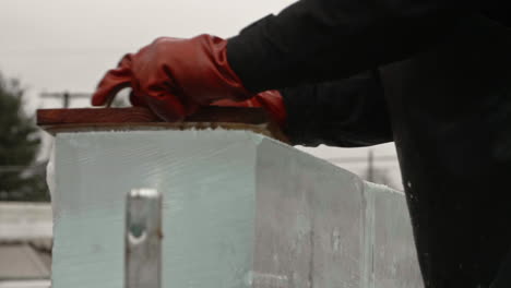 Slide-left-on-ice-sculptor-using-nail-board-to-shave-away-ice-block,-Slow-Motion