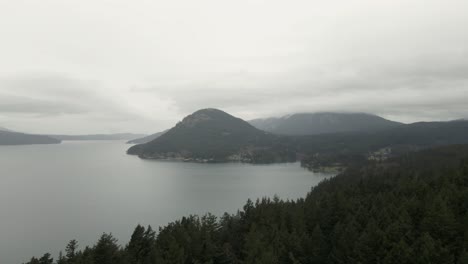 Misty-gray-skies-touch-the-tops-of-peaks-on-Orcas-Island,-Washington,-aerial-panorama