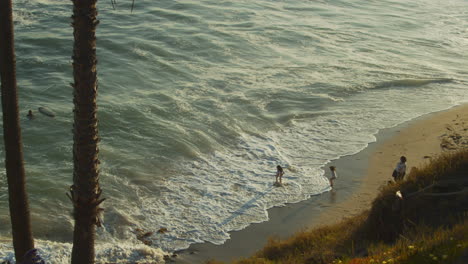 Young-children-at-a-Southern-California-beach-during-sunset-joyfully-play-in-the-gentle-ocean-waves-breaking-the-shoreline