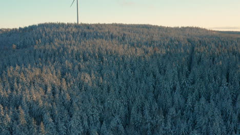 AERIAL---Wind-turbine-in-a-snowy-forest-at-sunrise-in-Sweden,-wide-shot-forward