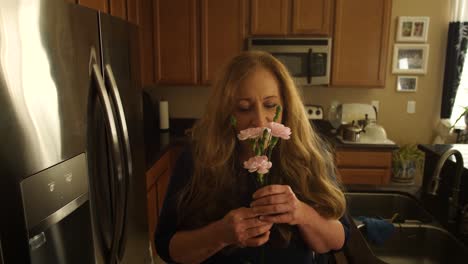 Red-haired-woman-smells-flowers-in-her-kitchen-smiling