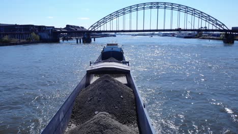 Dry-Bulk-Cargo-Barge---La-Primavera-Barge-With-Heaps-Of-Coal-Cruising-At-Noord-River-With-Arch-Bridge-In-Background-At-Hendrik-Ido-Ambacht,-Netherlands