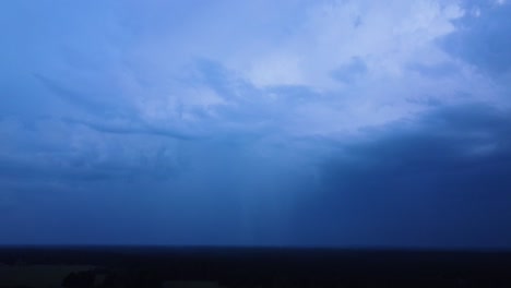 Beautiful-aerial-view-of-dramatic-dark-thunder-storm-clouds-in-summer-evening,-extreme-thunderstorm-with-several-lightning-strikes-deep-in-to-the-clouds,-distant-wide-angle-drone-shot-camera-tilt-down