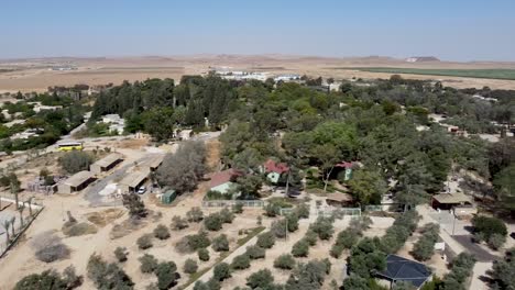Aerial-slide-to-the-right-drone-shot-of-a-panoramic-view-of-kibbutz-Sde-Boker-and-the-area-around-it,-filled-with-trees,-bushes,-fields,-trails,-buildings-and-houses