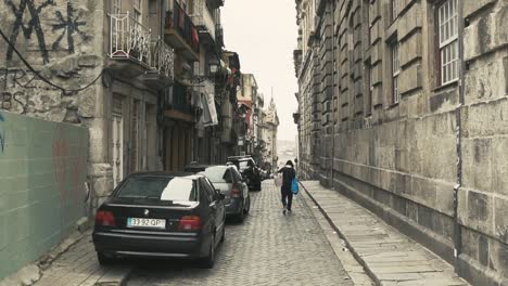 Man-carrying-bags-through-empty-and-old-side-street-in-Portugal-city-Porto