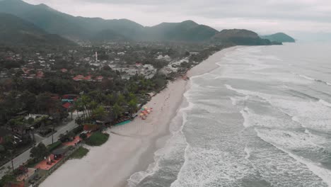 Lateral-drone-footage-of-the-beach,-mountain-and-houses-in-front-of-the-sea,-cloudy-day,-waves,-landscape-of-Juquehy,-Ubatuba,-northern-coast-of-SÃ£o-Paulo,-Brazil