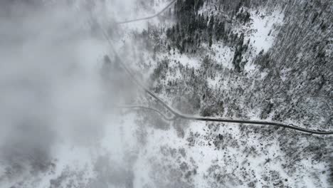 Aerial-forward-above-mountain-roads-snow-pine-trees-mist-fog-winter