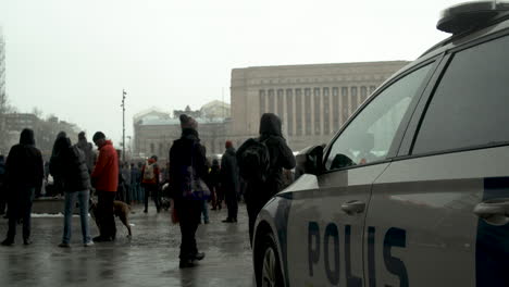 Wide-shot-of-a-Finland-police-car-on-the-streets-of-Helsinki-with-protesters-in-the-background,-cold-snowy-day
