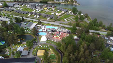 Mikkelparken-amusement-park-and-camping-location-in-Kinsarvik-Hardanger---Sideways-moving-aerial-with-tilt-up-to-show-both-theme-park-and-camping-close-to-river-and-fjord