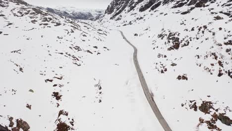 Dramatic-landscape-at-mountain-road-crossing-during-harsh-winter---unknown-car-passing-in-the-distant