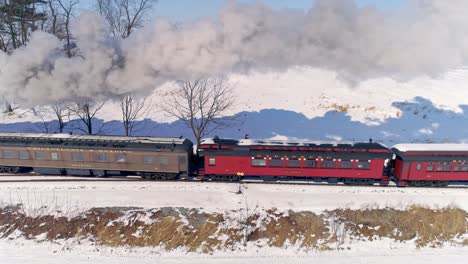 Aerial-View-of-an-Antique-Steam-Locomotive-Approaching-Pulling-Passenger-Cars-and-Blowing-Smoke-and-Steam-After-a-Snow-Storm