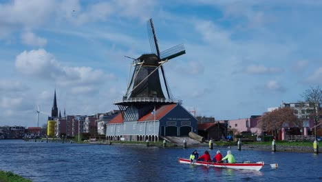 Menschen-Rudern-An-Der-Malerischen-Traditionellen-Hölzernen-Windmühle-In-Utrecht,-Niederlande,-Vorbei