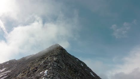 FPV-aerial-drone-flying-up-arrete-to-top-of-mountain-into-clouds-in-Swiss-Alps
