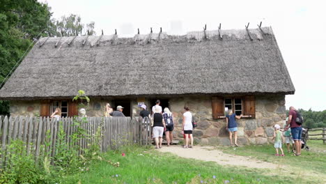 Crowd-standing-in-front-of-old-house-made-with-stones-and-thatched-roof-and-waiting-to-get-an-inside-view