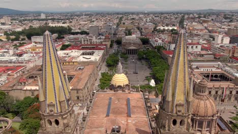 Luftaufnahme-Durch-Neugotische-Türme-Der-Kathedrale-Von-Guadalajara-In-Richtung-Plaza-De-La-Liberacion-In-Guadalajara,-Mexiko