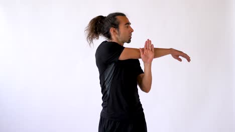 Long-Haired-Hispanic-Man-with-Goatee-Stretches-Shoulders-and-Arms-in-Front-of-White-Studio-Backdrop