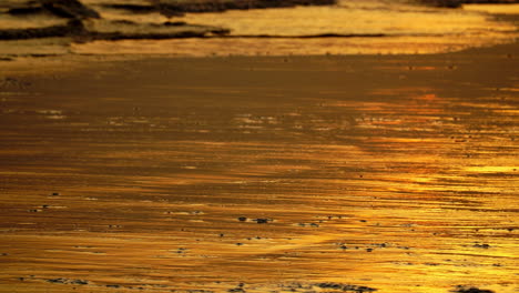 Ein-Orangefarbener,-Reflektierender-Sonnenuntergang,-Der-Am-Sandstrand-Leuchtet,-Während-Die-Verschmutzung-In-Die-Meereswellen-übergeht