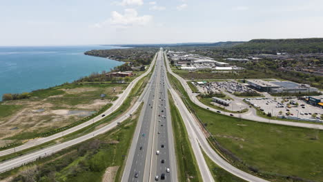 Aerial-flyover-traffic-on-highway-beside-Lake-Ontario-in-Canada-during-sunny-day