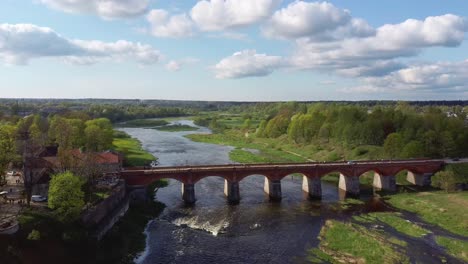 4k-Aerial-Clip,-Flying-Over-Small-City-of-Kuldiga-Latvia,-Red-Brick-Bridge-Over-River-Venta,-Wide-Waterfall
