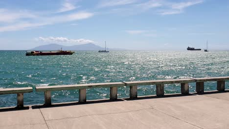Ein-Blick-Auf-Die-Tropische-Insel-Atauro-In-Der-Ferne-Am-Ufer-Mit-Meer-Und-Festgemachten-Booten-In-Der-Hauptstadt-Dili,-Timor-Leste,-Südostasien