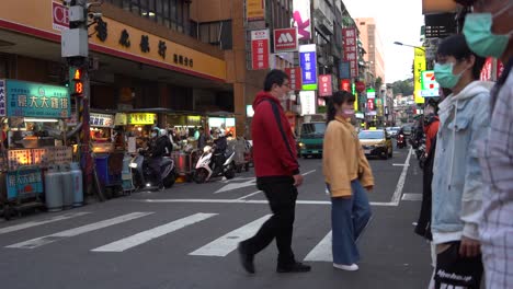 Yellow-taxi-passing-by-busy-street-at-Keelung-Taiwan,-and-pedestrians-wearing-masks-with-Covid-19-pandemic-awareness