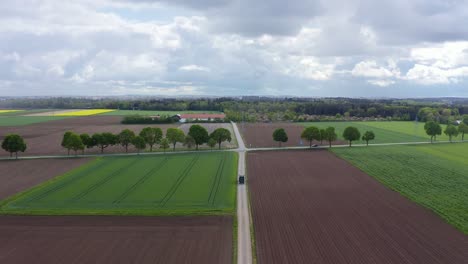 Landwirtschaftliche-Landschaft-Mit-Einem-Fahrenden-Traktor-Und-Der-Hohen-Winkelansicht-Einer-Drohne,-Die-Rückwärts-über-Bepflanzte-Und-Seltene-Felder-Fliegt