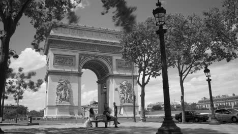 Schwarz-Weiß-Aufnahme-Von-Menschen-Und-Verkehr-An-Einem-Sonnigen-Tag-In-Paris,-Frankreich,-Mit-Dem-Berühmten-Arc-De-Triomphe-Im-Hintergrund