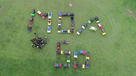 Moke-Owners-Association-50th-Anniversary-Convoy---Moke-owners-waving-toward-drone-acceding-directly-above-on-green-grass