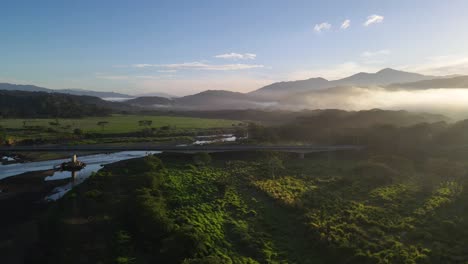 Drone-footage-of-sun-rising-behind-a-mountain-with-morning-haze-parallel-to-a-bridge