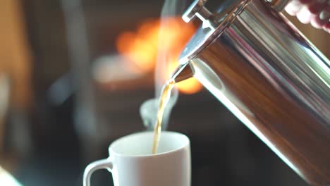 Slow-motion-pouring-steaming-hot-French-press-coffee-into-a-mug-in-front-of-a-glowing-fireplace