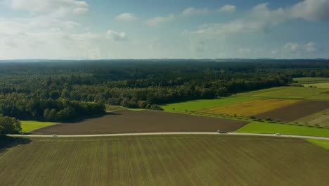 Rural-countryside-at-a-beautiful-day-at-the-end-of-the-summer-as-aerial-pullback-shot-with-a-road-and-driving-cars