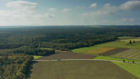 Wonderful-wide-aerial-view-over-a-landscape-of-fields,-woods-and-a-rural-placed-road-with-driving-cars,-concept-for-idyllic-traveling