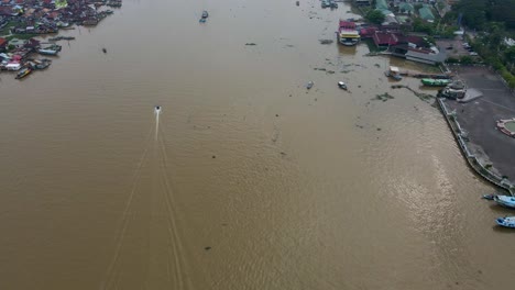 Motor-boat-speeding-on-Musi-river-in-city-of-Palembang,-aerial-drone-view