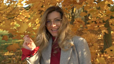 blond-woman-smiles-and-plays-with-yellow-and-golden-leaf-in-autumn-park