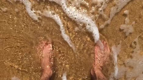 Close-up-shot-of-sea-water-moving-around-the-feet-of-a-man-on-a-sand-beach