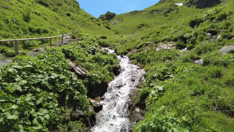 Small-waterfall-next-to-a-hiking-trail-in-a-green-mountain-landscape