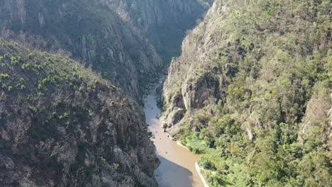 Aerial-descends-deep-rocky-canyon-to-group-of-rafters-on-Snowy-River