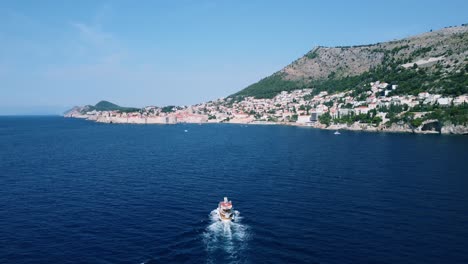 Toma-Aérea-Siguiendo-Un-Barco-Navegando-Hacia-El-Casco-Antiguo-De-Dubrovnik-En-Croacia.