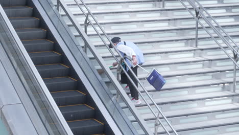 Shot-of-an-old-Japanese-cleaner-sweeping-the-staircase-outside-the-JR-Kanazawa-Station,-elderly-employment-in-Japan