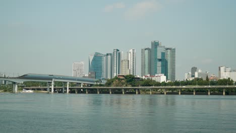 Dangsan-Railroad-Bridge-Over-Han-River,-Cars-Traffic-on-Gangbyeon-Express-Way,-Mecenatpolis-shopping-mall,-SEAH-Tower-and-KB-Insurance-skyscraper-on-blue-sky-background,-Hangang-riverfront,-Seoul